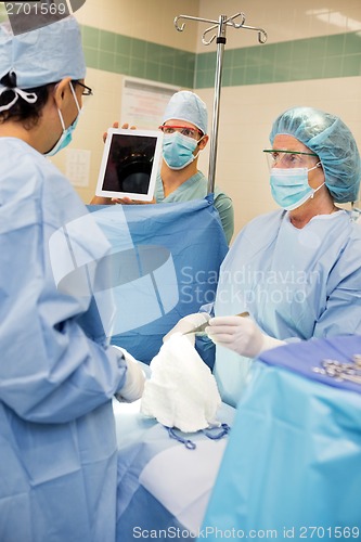 Image of Nurse Showing Digital Tablet To Doctor During Surgery