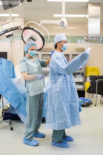 Image of Nurse Assisting Doctor In Wearing Operation Gown