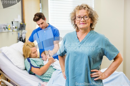 Image of Mature Nurse Standing With Couple And Newborn Baby In Background