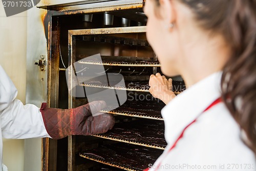 Image of Workers Removing Dried Meat Slices From Oven At Shop