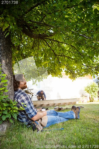 Image of Worker With Eyes Closed Leaning On Tree Trunk