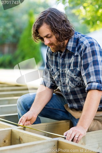 Image of Carpenter Measuring Wood With Tape At Construction Site