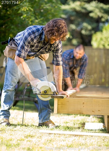 Image of Carpenter Cutting Wood With Handheld Saw While Coworker Assistin