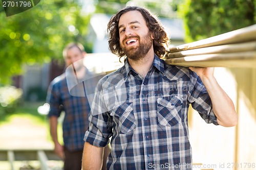 Image of Carpenter With Coworker Carrying Planks While Laughing