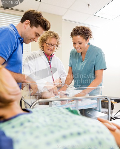 Image of Medical Team Examining Babygirl By Man With Mother In Foreground