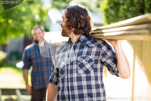 Image of Carpenter And Coworker Carrying Wooden Planks