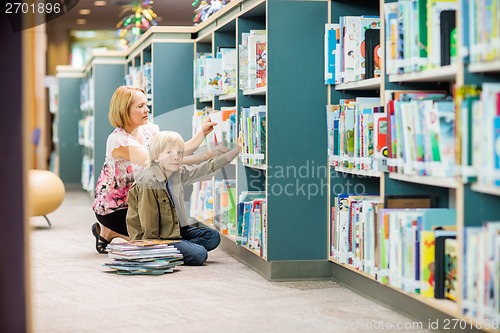 Image of Boy With Teacher Selecting Books From Bookshelf