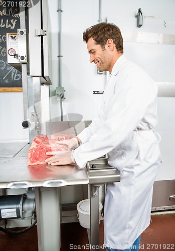 Image of Smiling Butcher Slicing Meat On Bandsaw