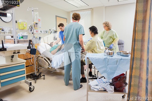 Image of Medical Team Operating Pregnant Woman While Husband Standing By