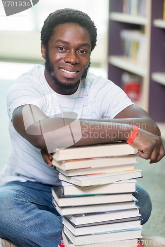 Image of Smiling Student With Stacked Books Sitting In Library