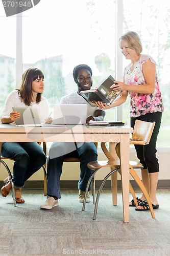 Image of Librarian And Students Looking At Book In Library