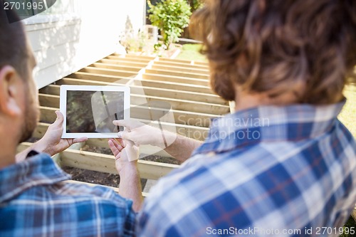Image of Carpenter Pointing At Digital Tablet While Coworker Holding It