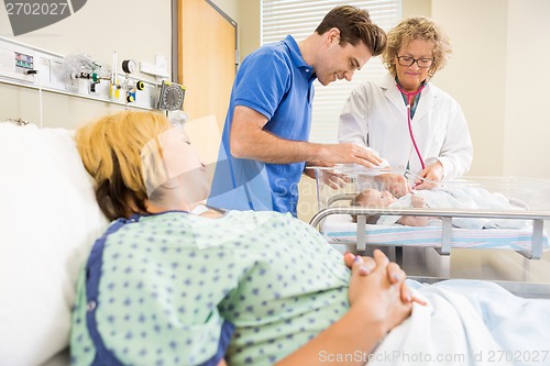 Image of Doctor Examining Newborn Baby While Parents Looking At Her