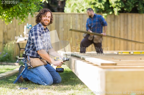 Image of Confident Worker Drilling Wood At Construction Site