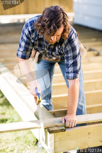 Image of Worker Cutting Wood With Saw At Construction Site