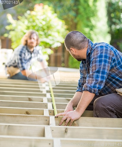 Image of Carpenters Measuring Wood With Tape At Site