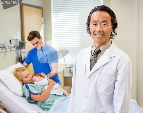 Image of Mature Doctor Standing With Couple And Newborn Baby In Backgroun