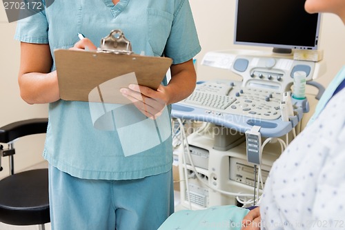 Image of Nurse Writing On Clipboard With Patient In Ultrasound Room