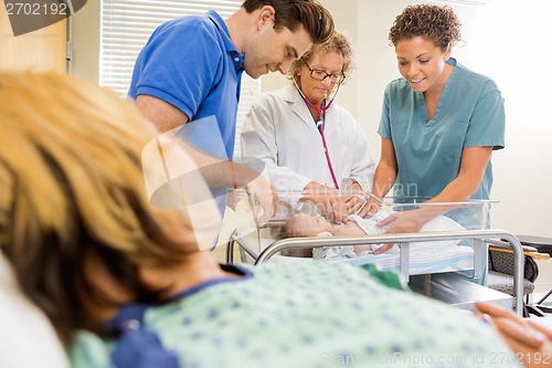 Image of Doctor Examining Baby By Nurse And Man With Mother In Foreground