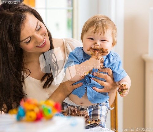 Image of Mother Holding Baby Boy Eating Cake With Icing On Face
