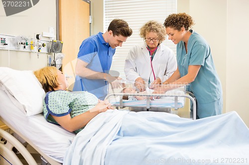 Image of Doctor Examining Baby While Parents And Nurse Looking At Her