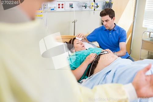 Image of Man Wiping Exhausted Pregnant Woman's Forehead In Hospital
