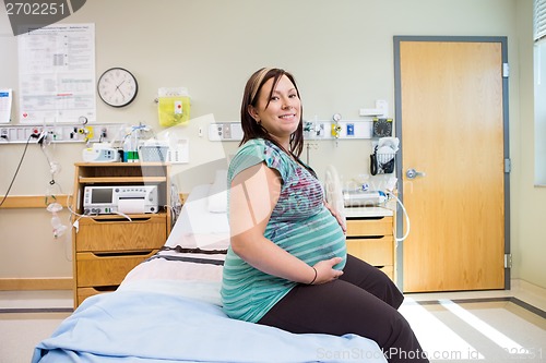 Image of Happy Pregnant Woman With Hands On Stomach On Hospital Bed