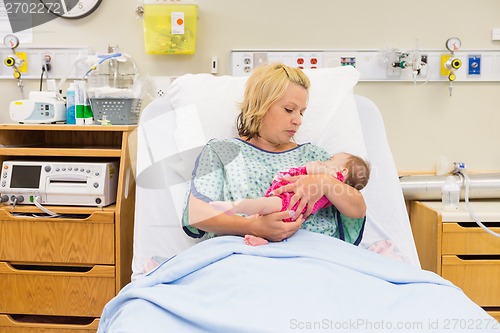 Image of Mother Looking At Newborn Baby Girl While Sitting On Bed