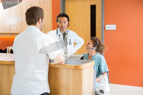 Image of Nurse Looking At Doctor Talking To Patient At Reception Desk