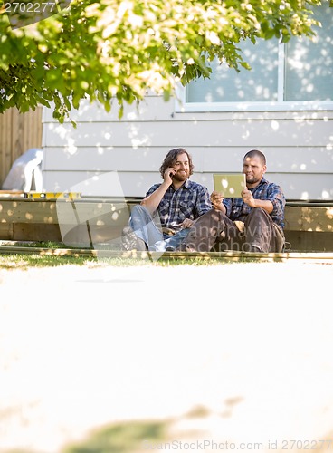 Image of Carpenter Using Digital Tablet While Coworker On Call At Site