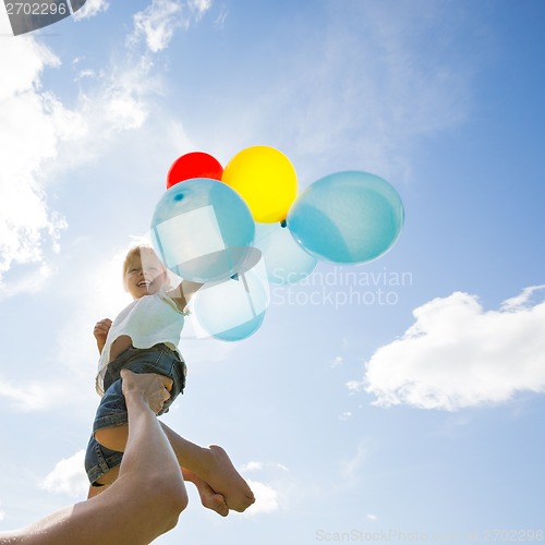 Image of Mother Lifting Daughter Holding Balloons Against Cloudy Sky