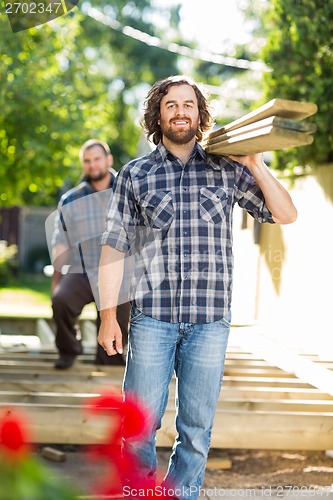 Image of Carpenter And Coworker Carrying Wooden Planks At Construction Si