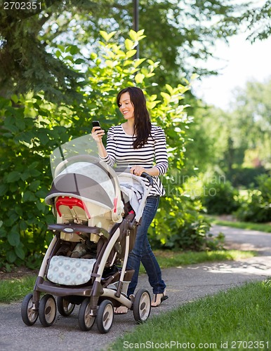 Image of Woman With Baby Carriage Using Cell Phone In Park