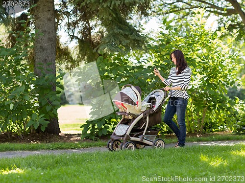 Image of Woman With Baby Carriage Using Cell Phone In Park