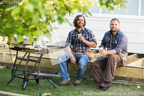 Image of Workers Holding Disposable Cups While Sitting On Wooden Frame