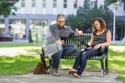 Image of Students Using Digital Tablet On Bench At Campus