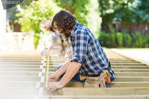 Image of Mid Adult Carpenters Measuring Wood With Tape