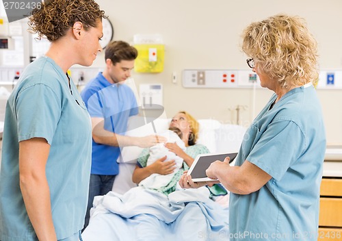 Image of Nurses Discussing Report On Digital Tablet Against Couple With B