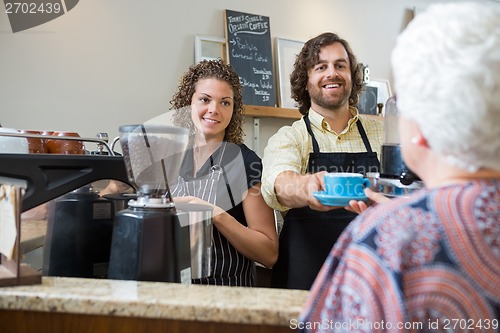 Image of Cafe Owners Serving Coffee To Woman At Counter