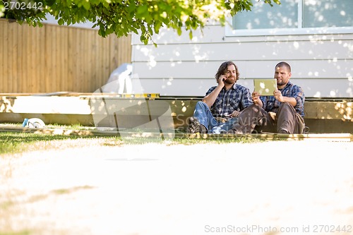 Image of Worker Using Digital Tablet While Coworker On Call At Site