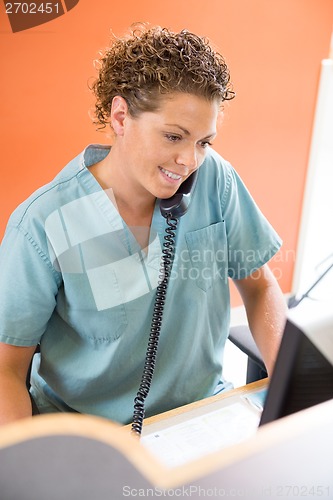 Image of Nurse Answering Telephone While Working At Reception Desk
