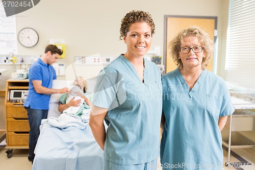 Image of Confident Nurses Standing Against Couple With Baby In Background