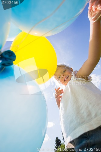 Image of Happy Girl Holding Balloons Against Sky