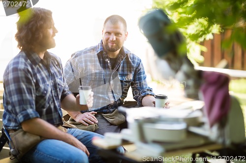 Image of Carpenter With Coworker Holding Disposable Coffee Cup At Site