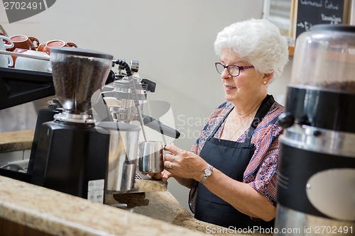 Image of Senior Waitress Steaming Milk In Cafe