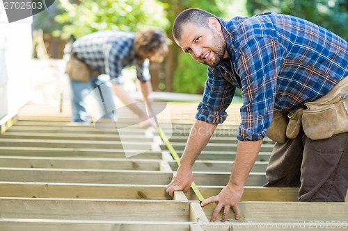 Image of Carpenter Measuring Wood With Tape While Coworker Assisting Him