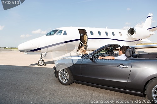 Image of Pilot In Convertible Parked Against Private Jet