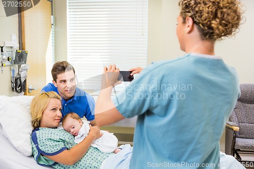 Image of Nurse Photographing Couple With Newborn Baby Through Cellphone