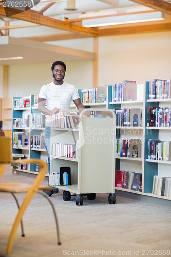 Image of Librarian With Trolley Of Books Smiling In Bookstore