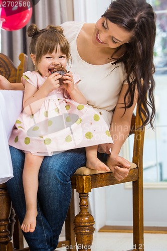 Image of Girl Eating Cupcake While Sitting On Mother's Lap